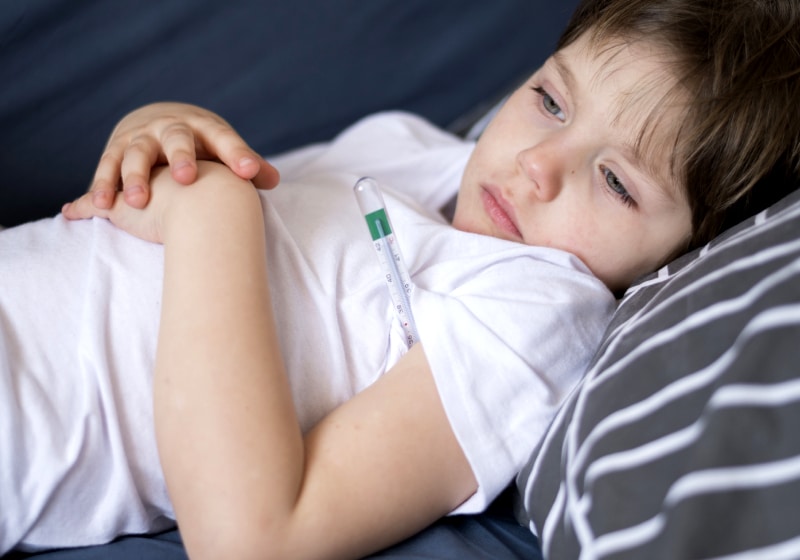 vista frontal criança deitada na cama doente com termômetro no em baixo de braço 