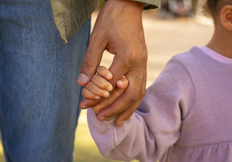 close up na mão de pai segurando mão da filha andando ao ar livre 