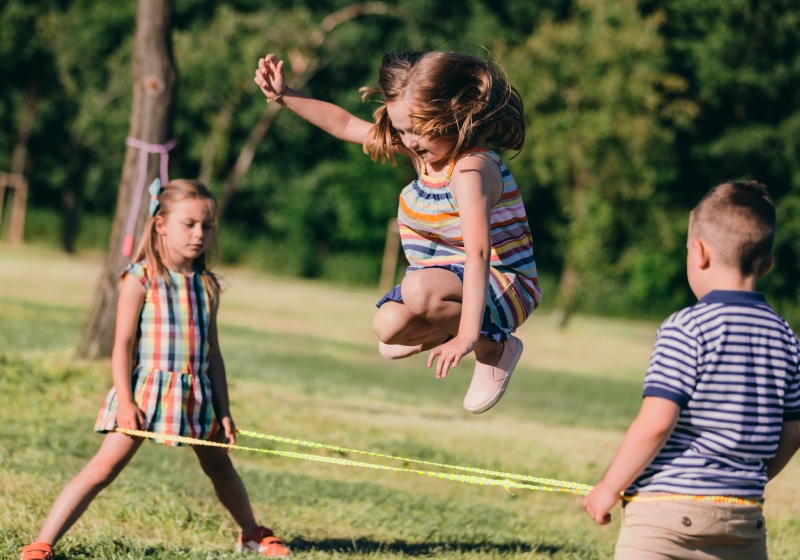 garotinha pulando pelo elástico brincadeira e um menino e uma outra menina segurando elástico ao ar livre 
