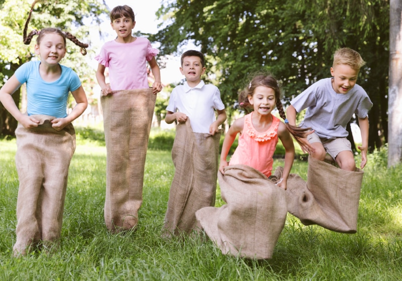 crianças brincando de corrida do saco no campo ao ar livre 