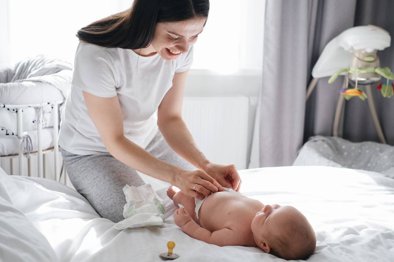 mãe sorrindo fazendo massagem no bebê em cima da cama