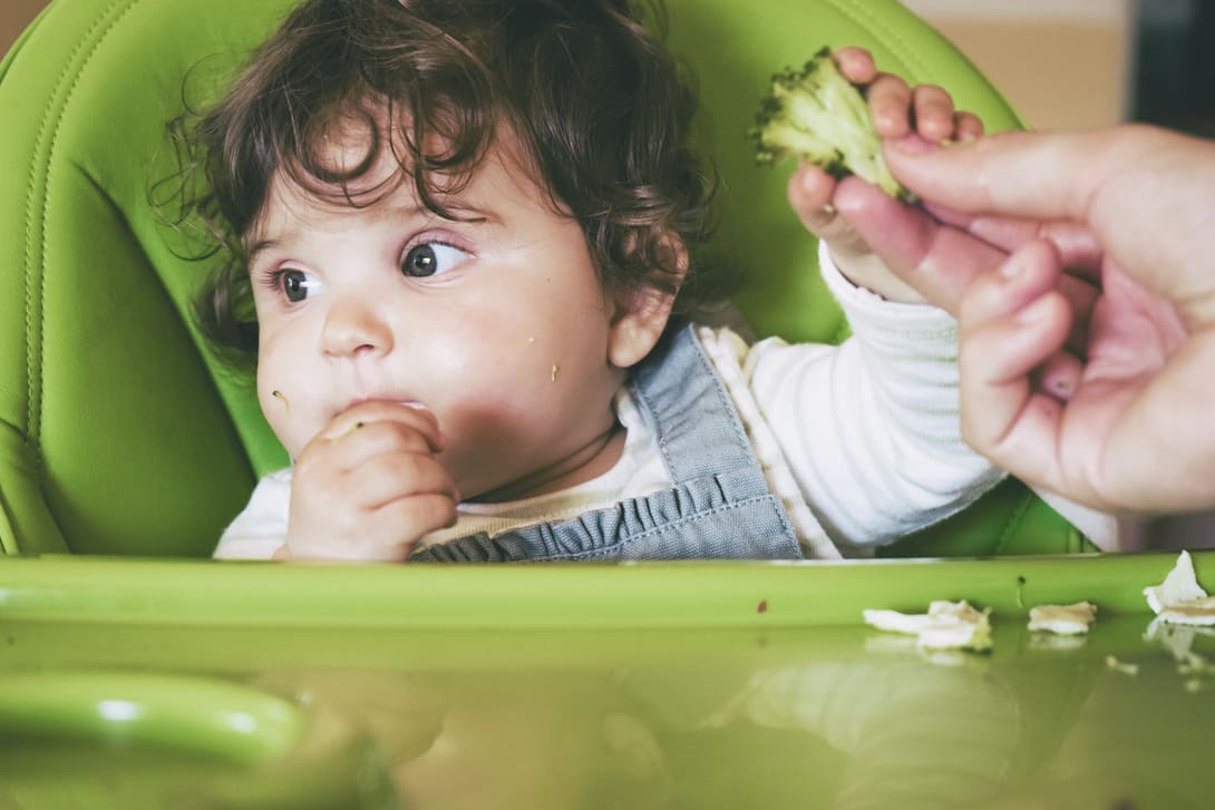 bebê na cadeirinha de alimentação comendo brócolis