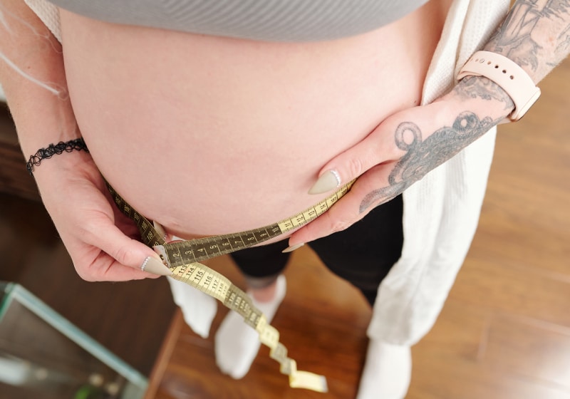 vista de cima de mulher gravida medindo sua barriga com fita 