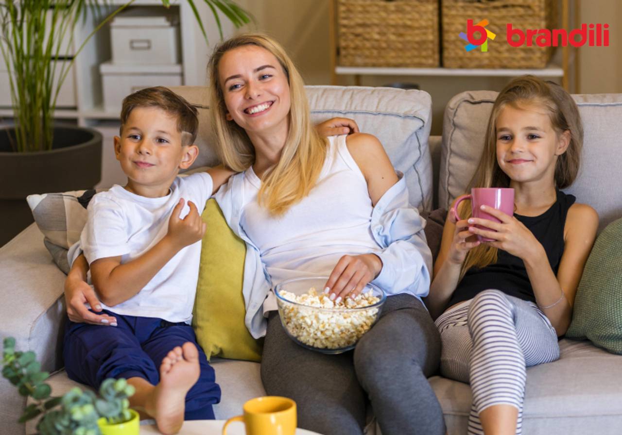 mãe e seus filho comendo pipoca no sofá da sala assistindo um filme 