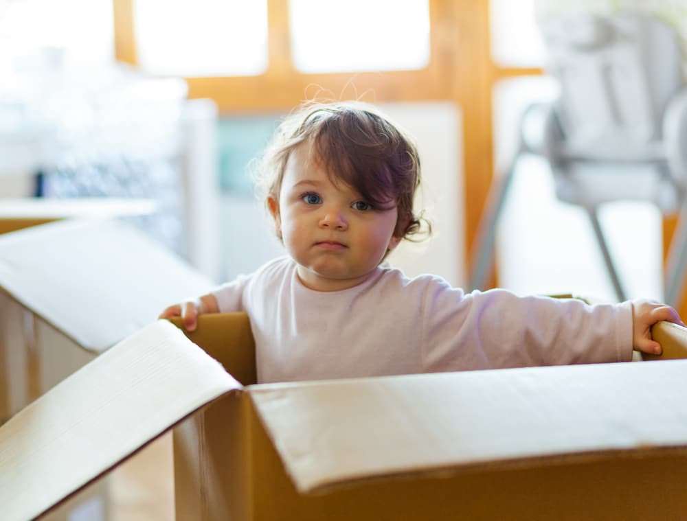 menina de dois anos em uma caixa de papelão com cara fechada