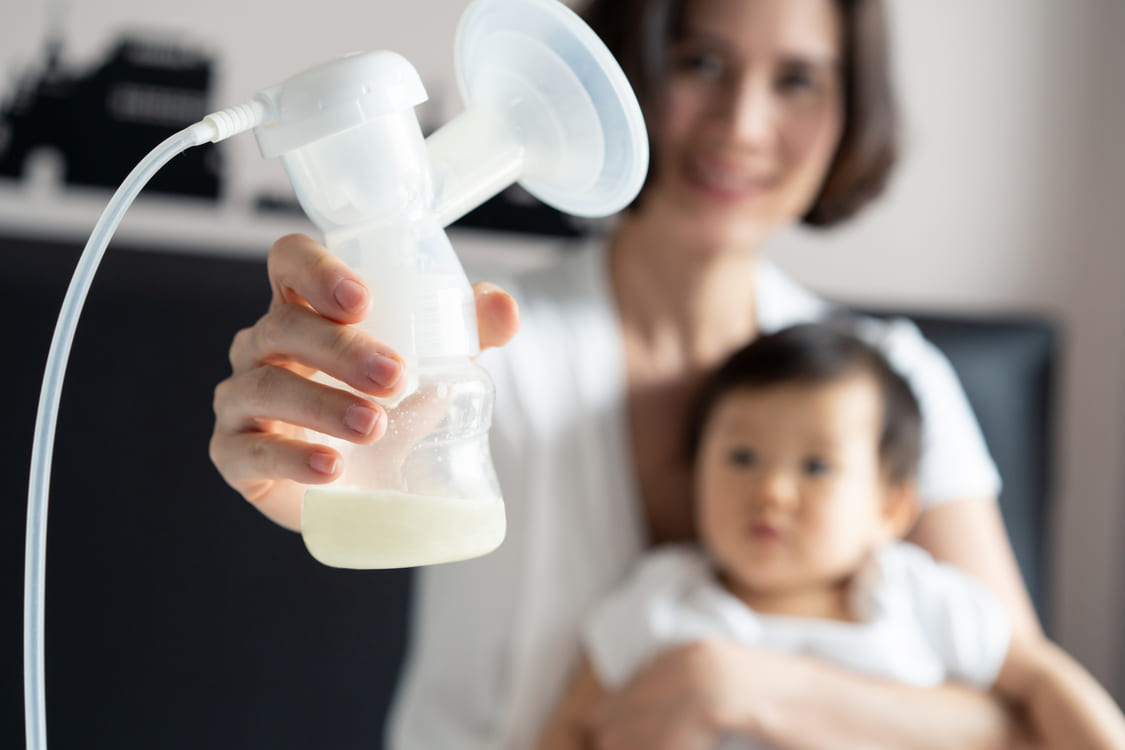 mãe tirando leite materno com um bebê no colo