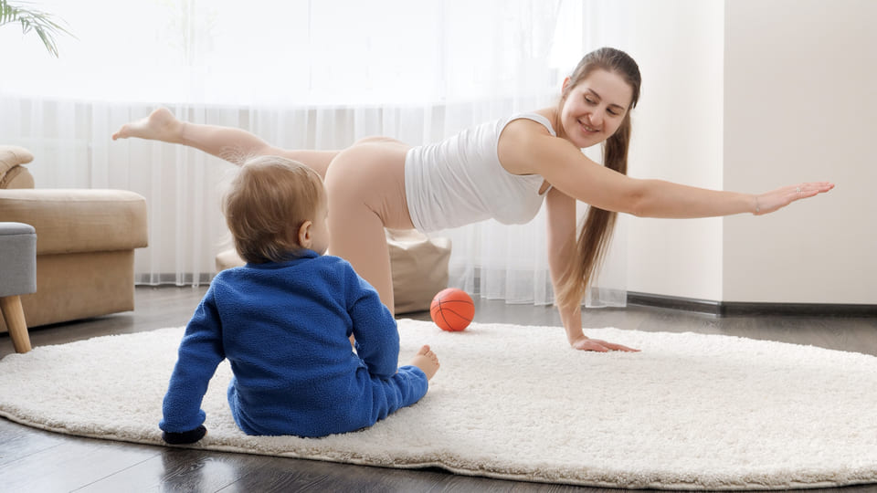mãe praticando exercicios físicos em casa ao lado do bebê