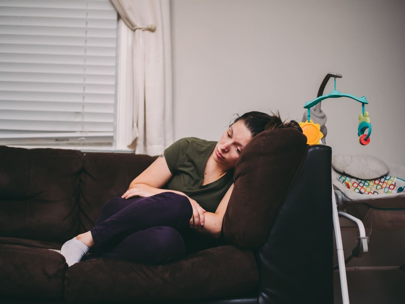 mulher apática deitada no sofá ao lado de um berço