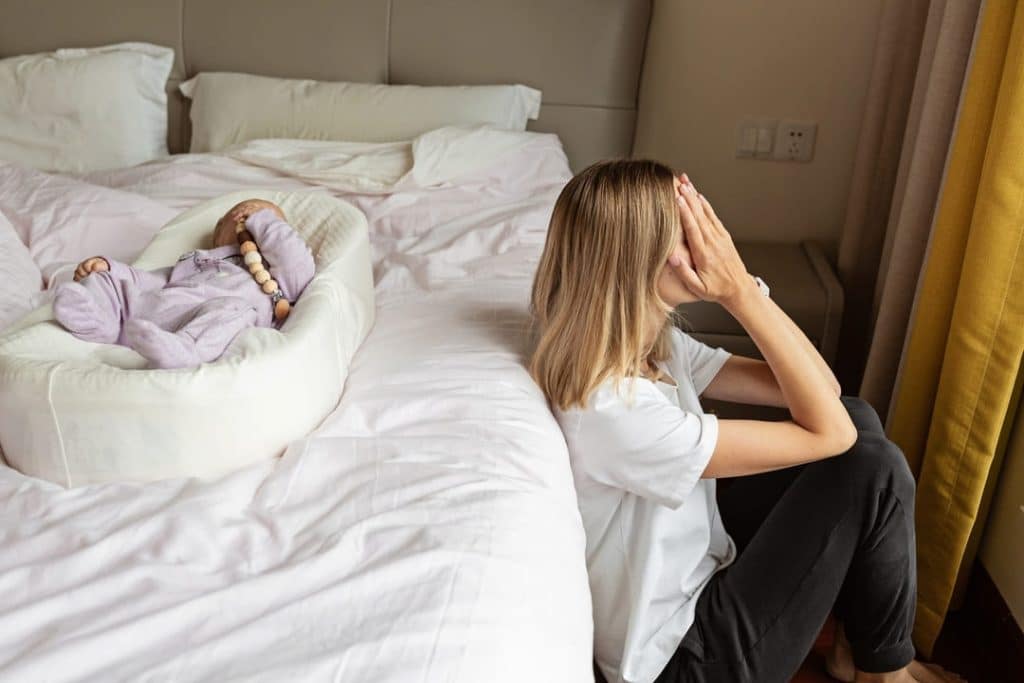 mulher com depressão pós-parto sentada ao lado da cama