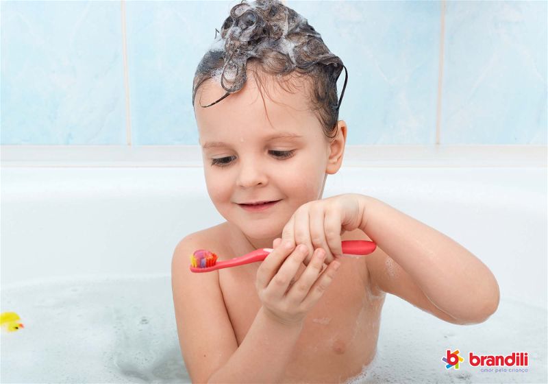 criança tomando banho segurando escova de dente