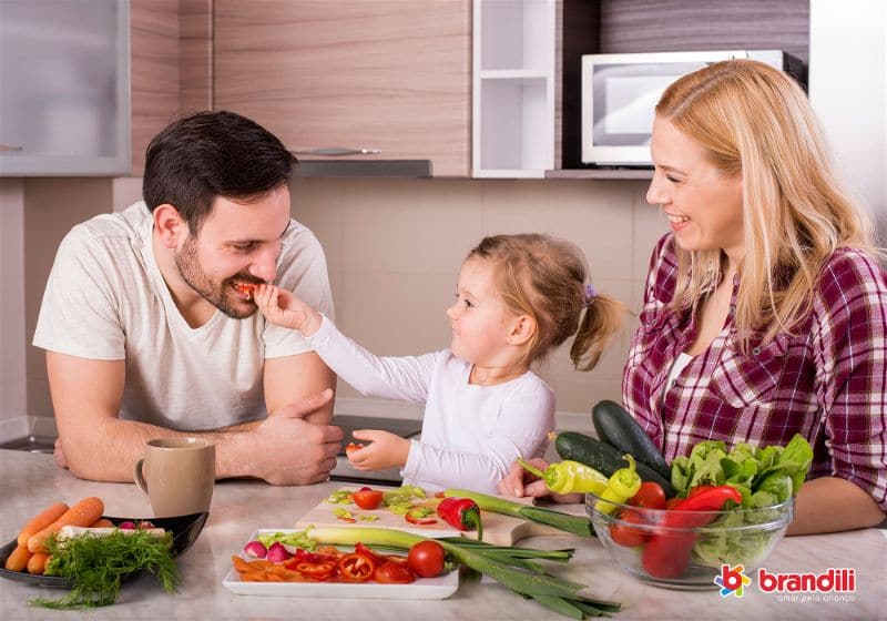 Pai, filha e mãe preparando legumes na cozinha