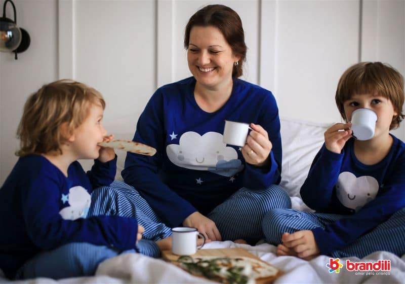 Mãe e dois filhos meninos sentados de pijama tomando café da manhã
