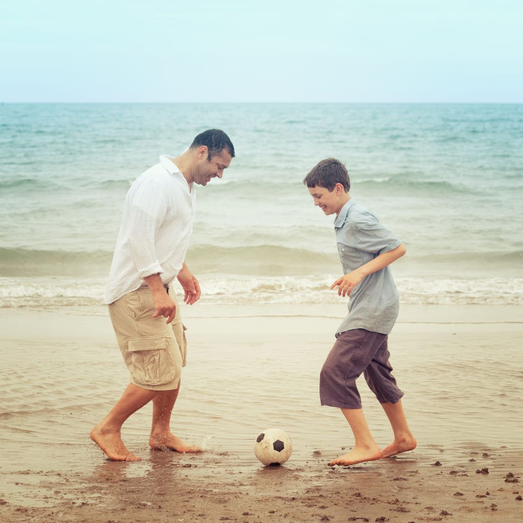 pai e filho jogando bola na areia da praia