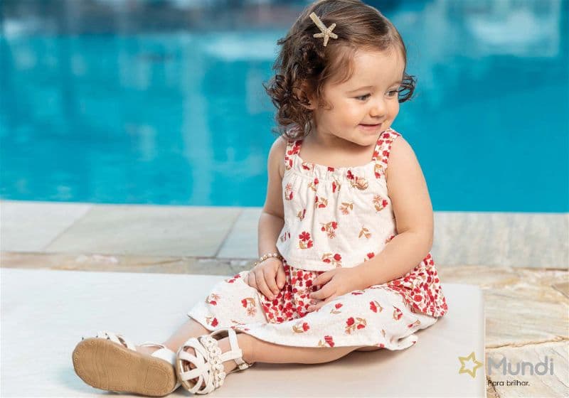 Menina bebê sentada com um vestido florido em frente a uma piscina
