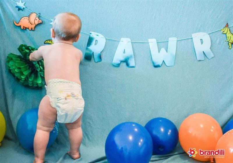 Bebê usa fralda descartável enquanto brinca num varal com a palavra RAWR