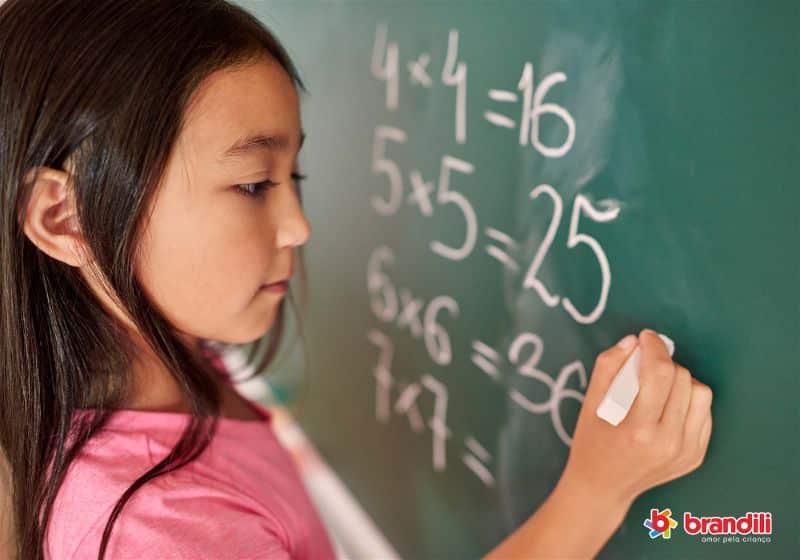 criança resolvendo conta de matemática no quadro escolar