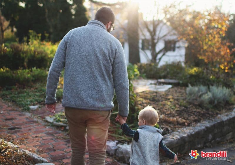 Pai segurando o filho pela mão enquanto caminham num jardim