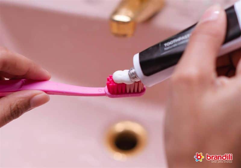 mãos segurando uma escova de dente inserindo pasta 