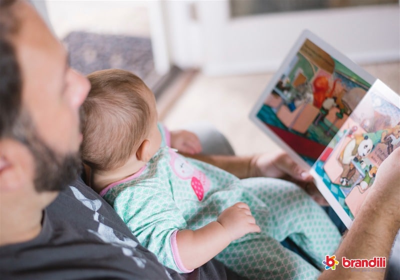 Foto de um pai lendo um livro infantil com um bebê em seu colo