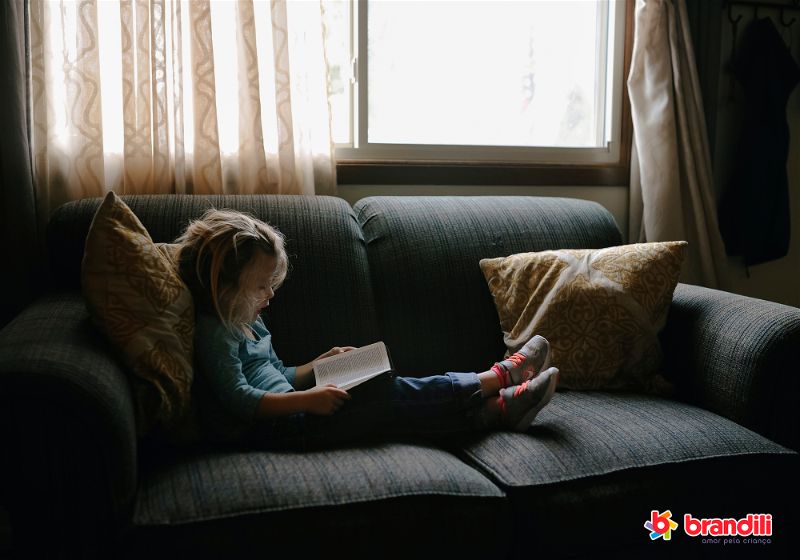menina lendo livro no sofá
