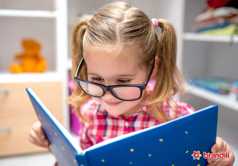 Menina usa óculos de grau enquanto lê um livro azul