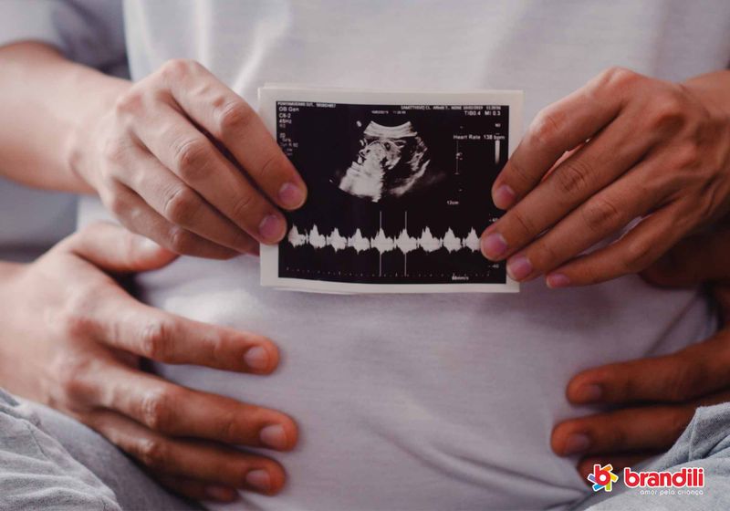 Mãe e pai abraçados segurando foto de ultrassom em frente à barriga