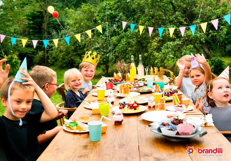 crianças sentadas a mesa com decorações de aniversário e doces postos na mesa