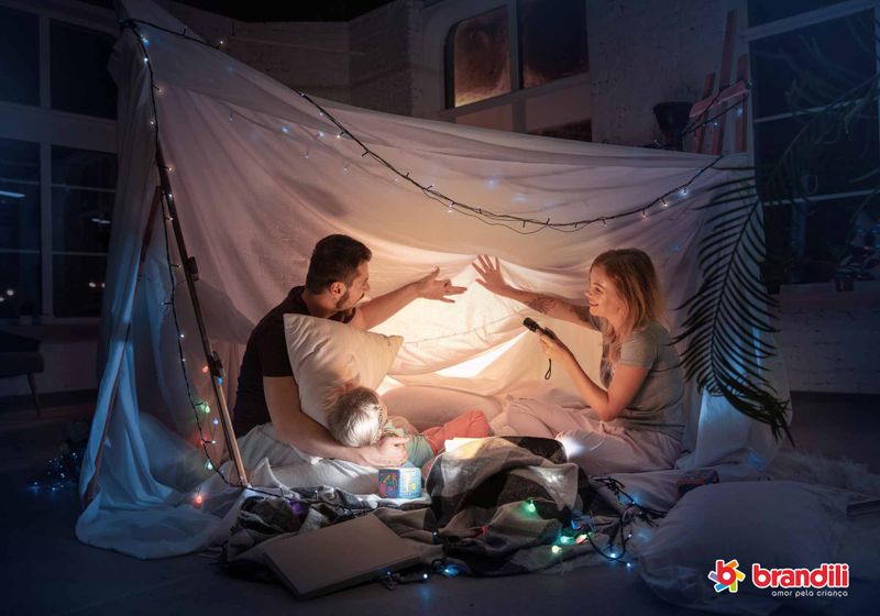 Pai, mãe e filha brincam de cabana com luzes em casa.