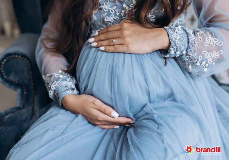 Mulher vestindo vestido azul segurando a barriga grávida;