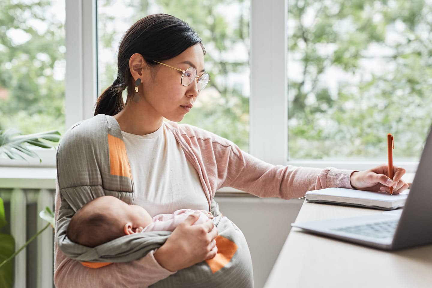 mãe sentada em frente do computador com bebê no colo 