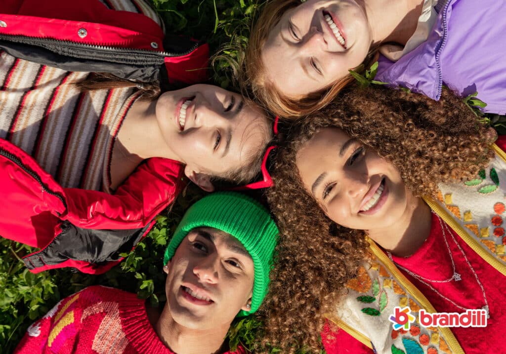 Três meninas e um menino adolescente deitados na grama em círculo sorrindo