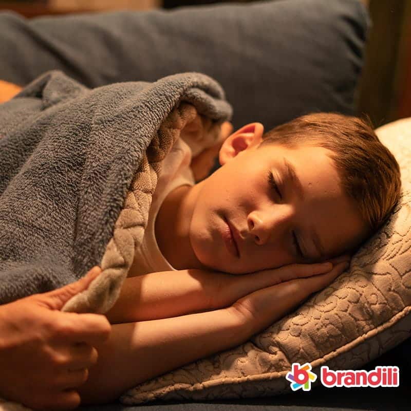 garoto dormindo calmamente enquanto uma mão o cobre com um cobertor