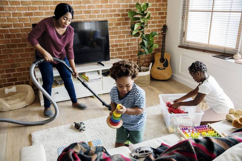 mãe passa aspirador na casa enquanto filhos arrumam os brinquedos