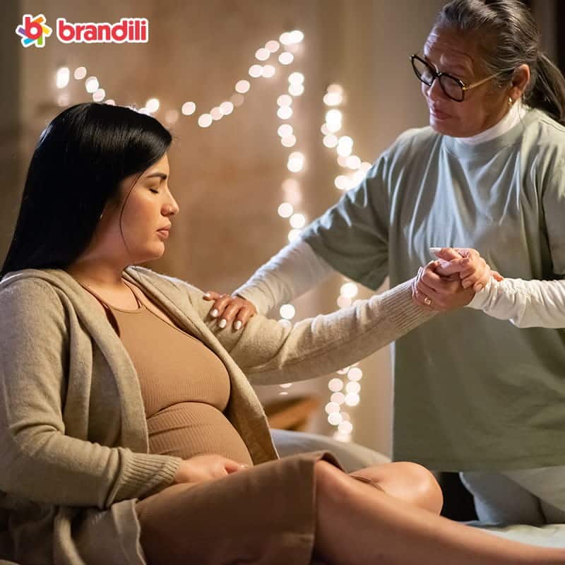 mulher gravida e parteirar em roupas casuais sentada na cama doula segurando a mao