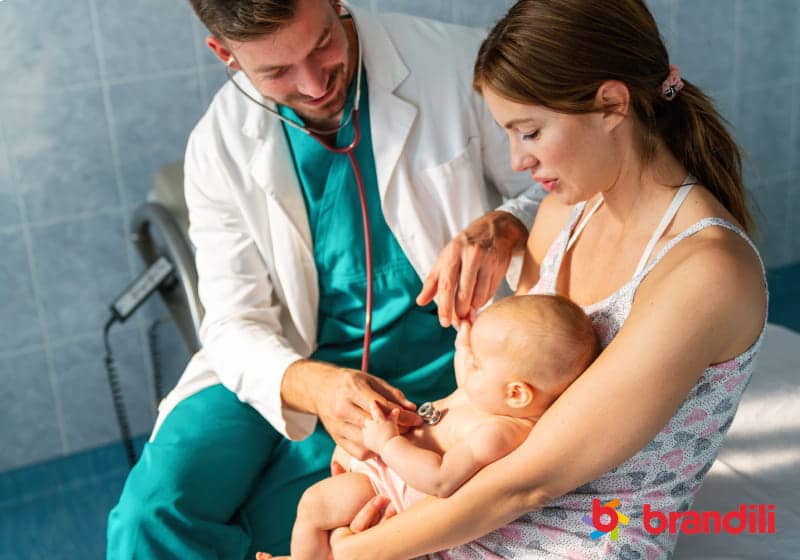 pediatra médico examina bebê no colo da mãe sentados na cama com estetoscópio