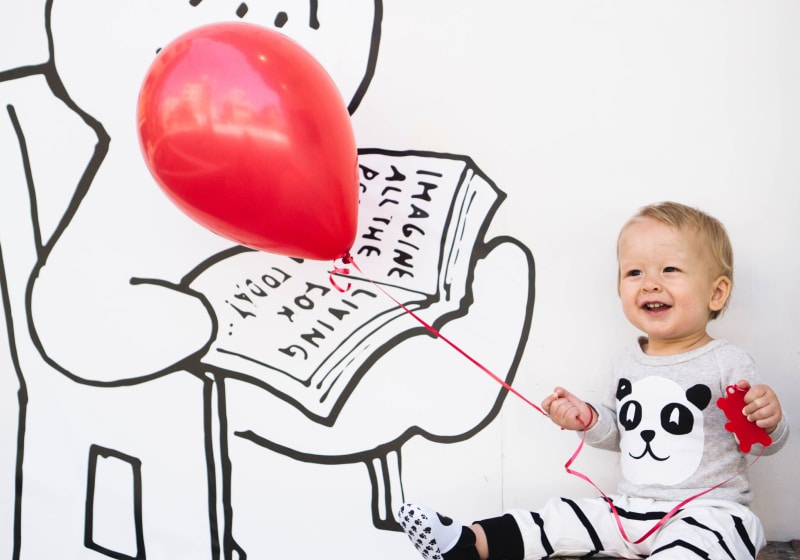 bebe sentado sorridente segurando um balão vermelho pela cordinha 