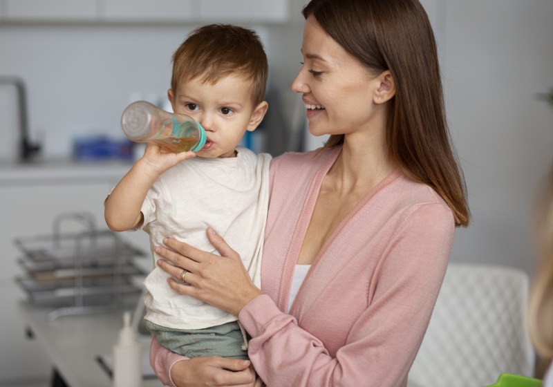 imagem de mulher segurando uma criança bebendo suco em uma mamadeira 