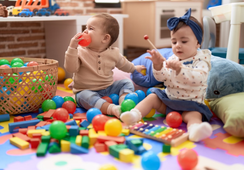 duas criancas brincando com bolas e xilofone sentada no tapete com almofadas da brinquedoteca 