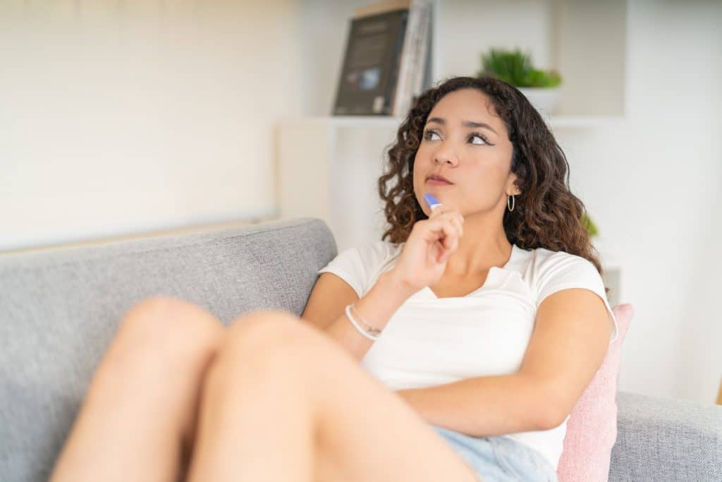 mulher sentada no sofá com um teste de gravidez e uma expressão de dúvida