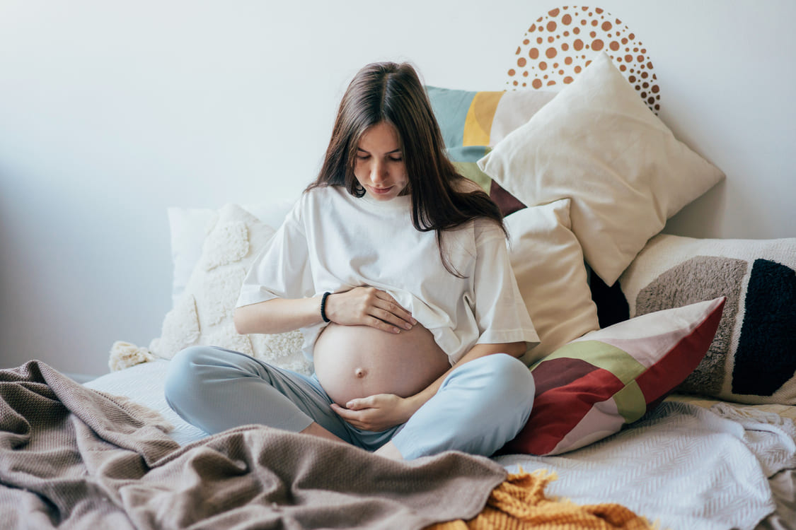 mulher grávida sentada na cama com a mão na barriga 