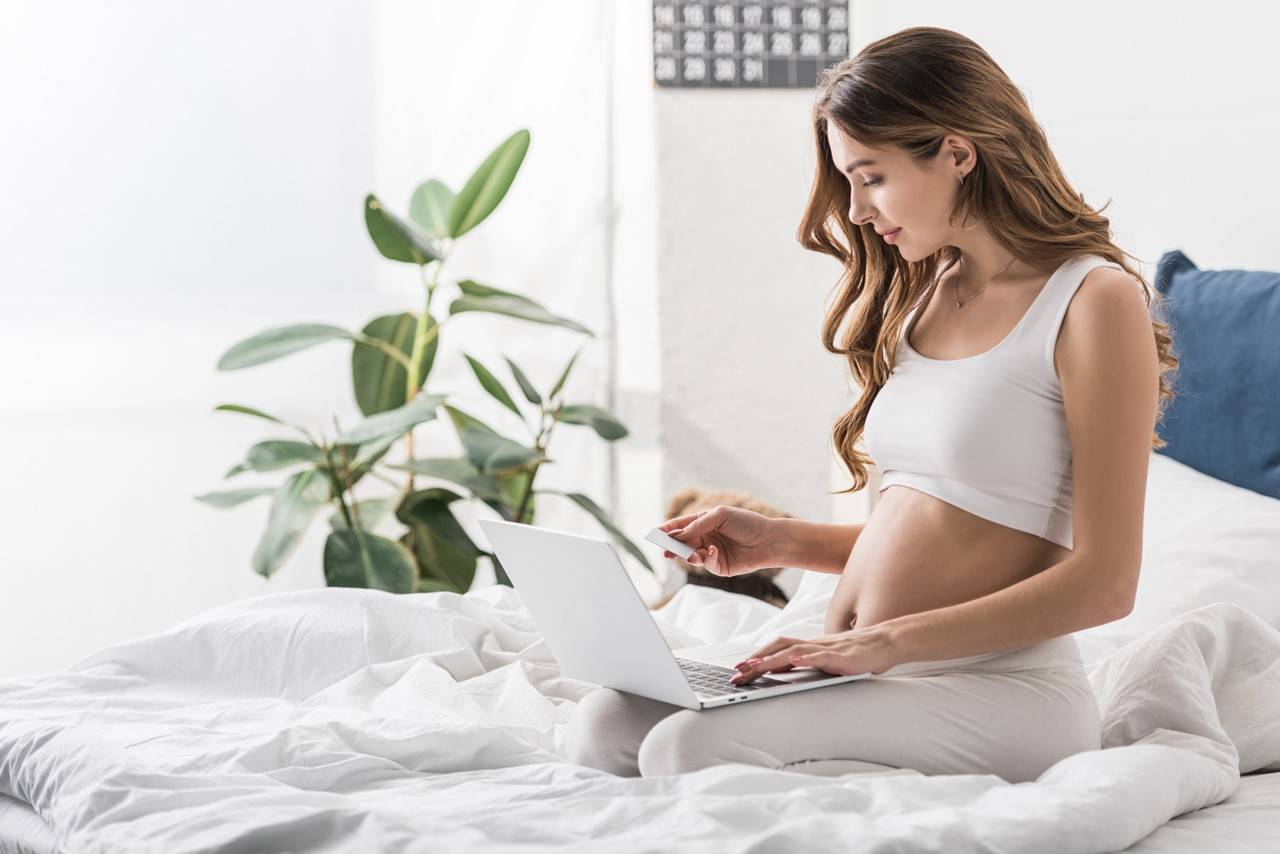 grávida de cinco semanas sentada na cama usando o computador