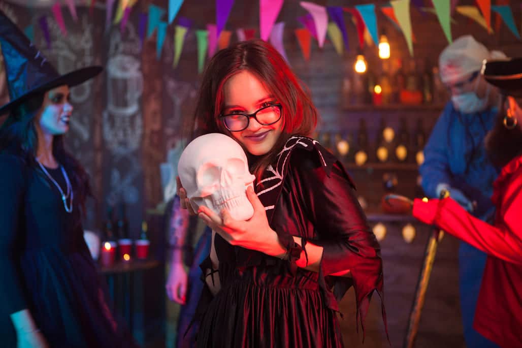 menina segurando uma caveira de mentira em um fundo com decoração de hallowen