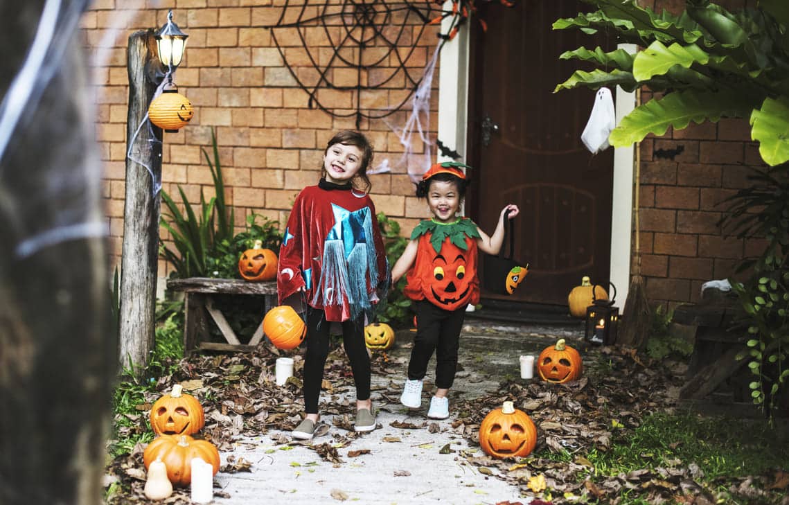 crianças fantasiadas em pé na frente de uma casa enfeitada para o hallowen