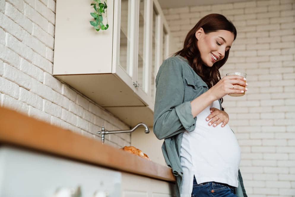 grávida de 7 semanas encostada no balcão da cozinha bebendo água