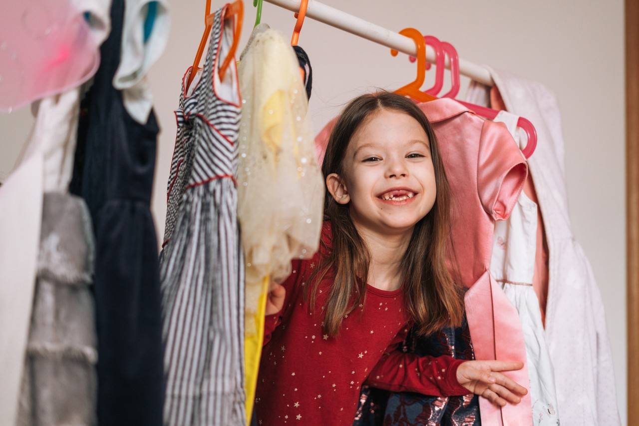 criança feliz no meio de vários vestidos 