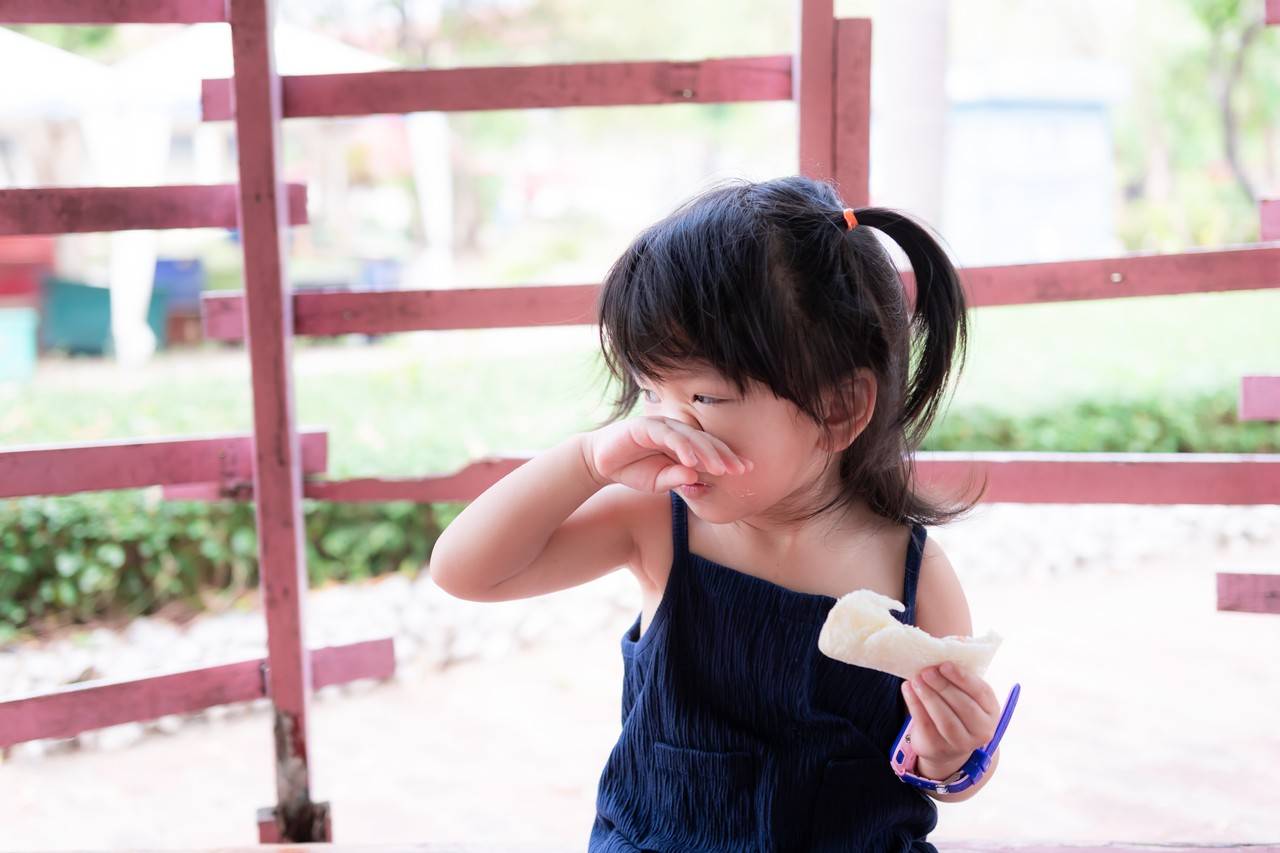 menina coça o nariz enquanto brinca ao ar livre