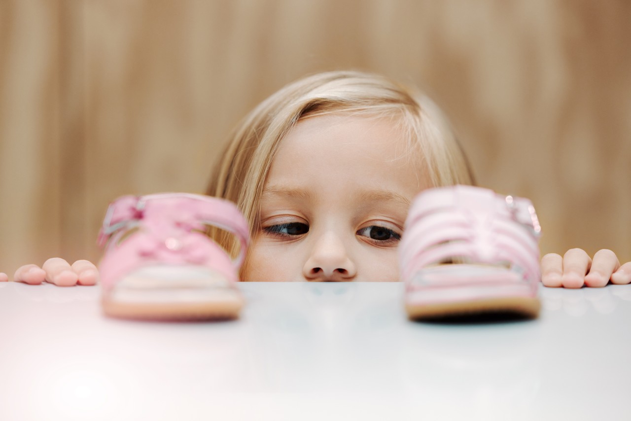 criança pequena olhando para dois calçados sob uma mesa