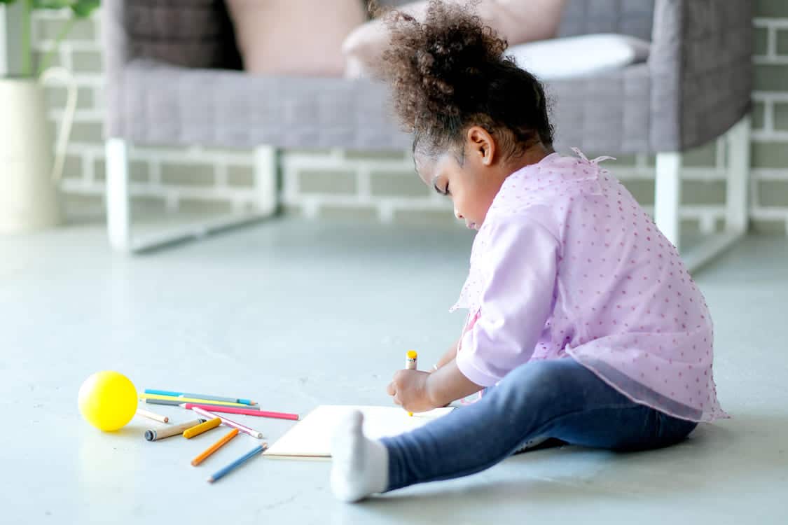 menina usa lápis de cor para pintar enquanto senta no chão