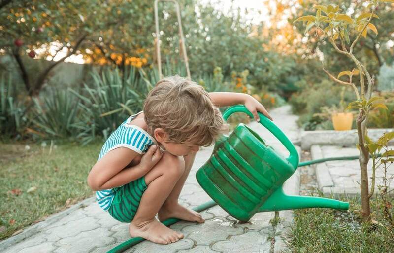 Criança agachada em jardim, segurando regador de cor verde