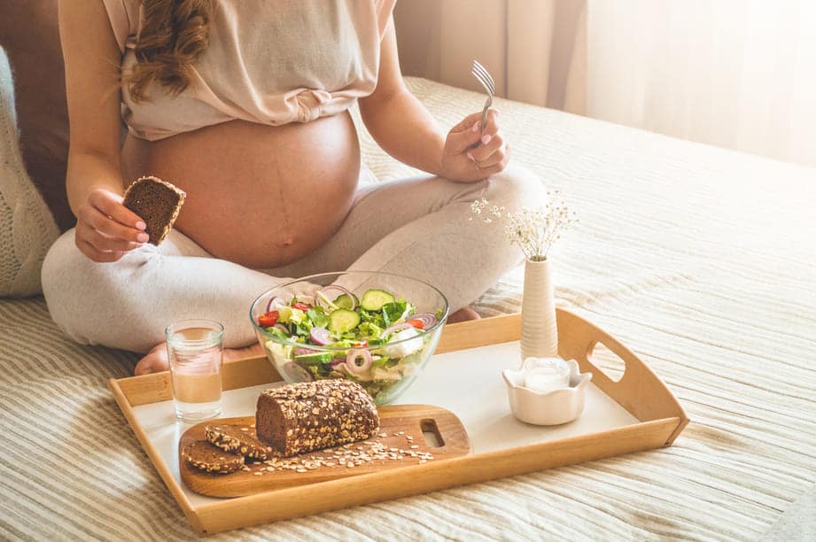mulher grávida sentada na cama comendo pão integral 